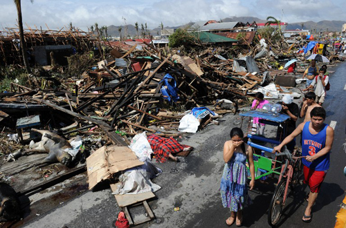 [Caption]esidents walk past destroyed houses and dead bodies littered along a road in Tacloban, on the eastern island of Leyte on November 10, 2013 after Super Typhoon Haiyan swept over the Philippines